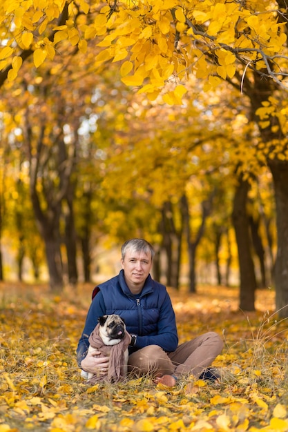 Een man met zijn geliefde mopshond op een wandeling in de herfst in het park