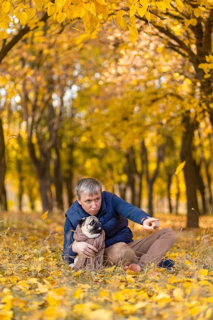 Een man met zijn geliefde mopshond op een wandeling in de herfst in het park