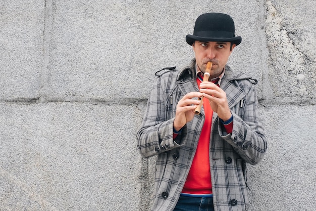 Een man-muzikant speelt een houten instrument op straat tegen een grijze muur Stedelijke levensstijl