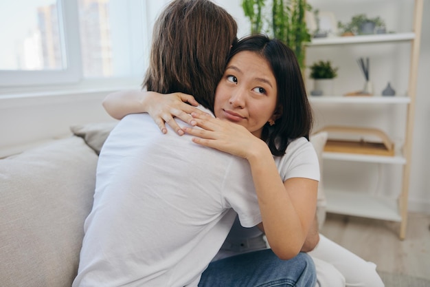 Een man omhelst zijn Aziatische vriendin thuis Psychologische ondersteuning voor een vriend