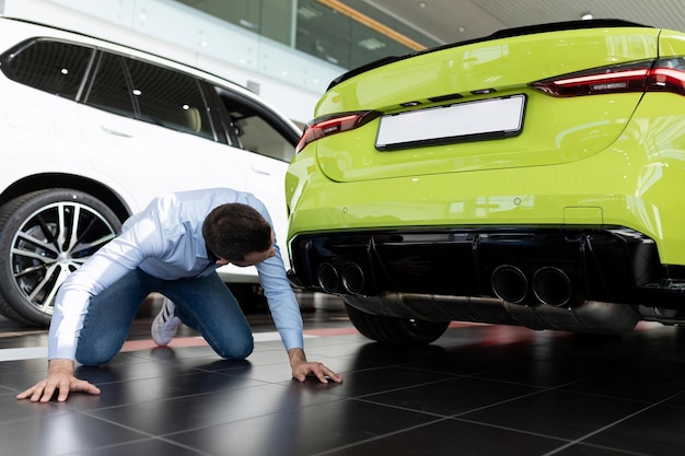 Een man onderzoekt in detail het uitlaatsysteem van een nieuwe auto in een autodealer