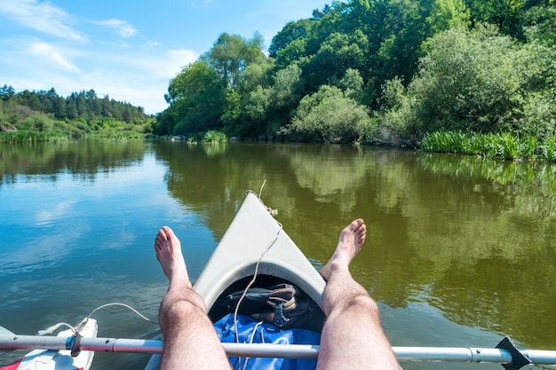 Een man ontspannen op kajak aan de rivier. landschap met blauw water en groene bomen