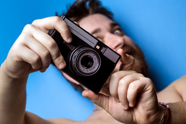 Een man op een blauw oppervlak, met een oude camera in zijn handen en doet alsof hij fotografeert