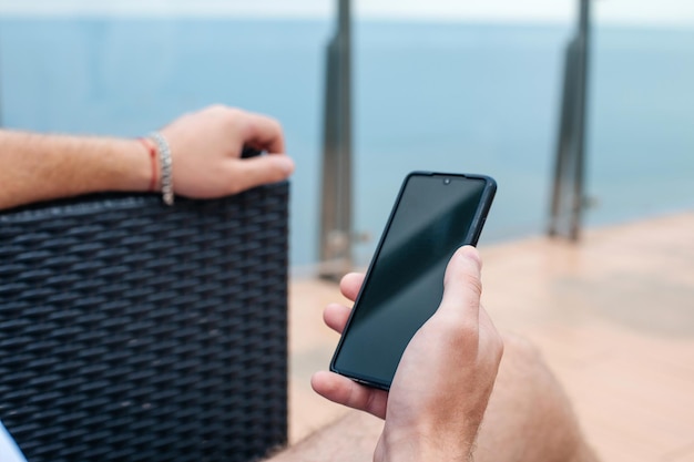 Foto een man op een zomerterras bij de zee houdt een telefoon in zijn handen