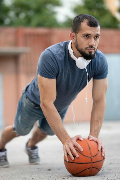 Foto een man op straat doet push-ups, leunend op een basketbal