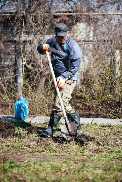 Een man plant een jonge boom De boer graaft de grond met een schop voor een kleine zaailing Het concept van bescherming van het milieu en ecologie