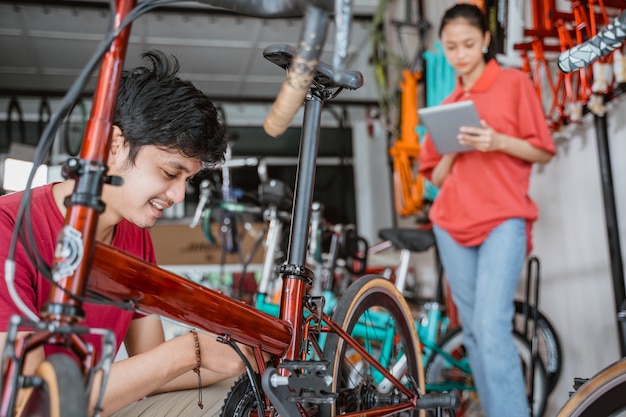 Een man repareert een fiets met een vrouw op de achtergrond met behulp van een digitale pad