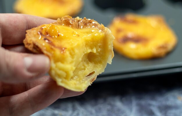 Foto een man's hand houdt een halve been gebeten verse portugese pastel de nata taart met custard op de