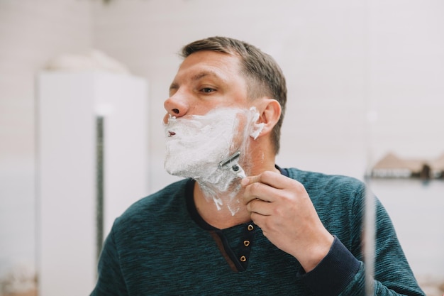 Een man scheert zijn baard voor een spiegel in zijn badkamer.