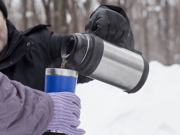 Een man schenkt thee aan een vrouw uit een thermoskan in een thermosbeker om te drinken en op te warmen.