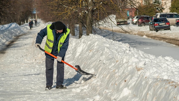 Een man schept sneeuw van een weg.