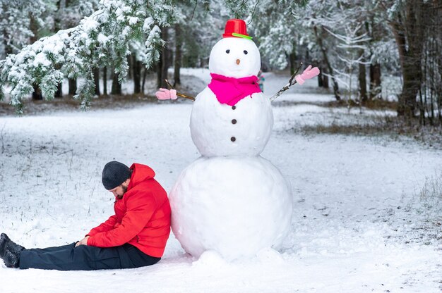 Een man slaapt bij een grote sneeuwpop in een besneeuwd bos