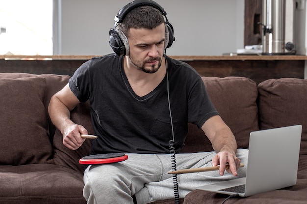 Een man speelt de trommel en kijkt naar het laptopscherm. Het concept van online muzieklessen, lessen videoconferenties.