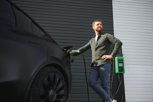 Een man staat bij een oplaadstation en laadt zijn elektrische auto op