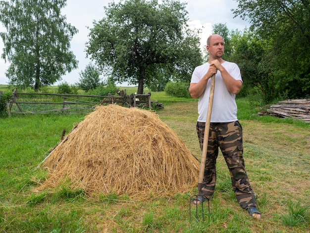 Een man staat met zijn rug naar de camera met een hooivork voor een hooiberg Landelijk landschap voorbereiding van diervoeder Landelijk leven