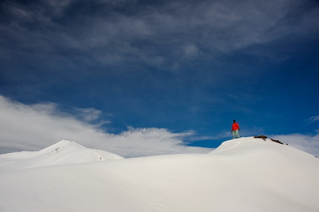 Een man staat op de met sneeuw bedekte berg, tegen de lucht