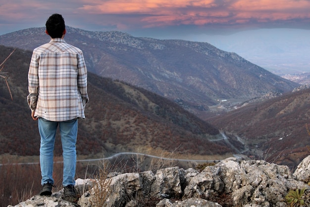 Een man staat op een bergtop en kijkt uit over een bochtige weg.