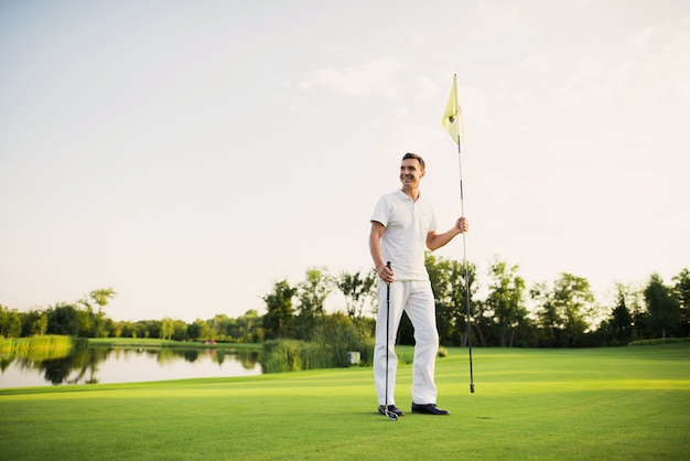 Een man staat op een golfbaan, heeft een golfclub en een vlag