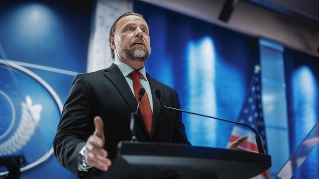 Foto een man staat op een podium met een bord waarop 'u' staat. s. ministerie van staat '