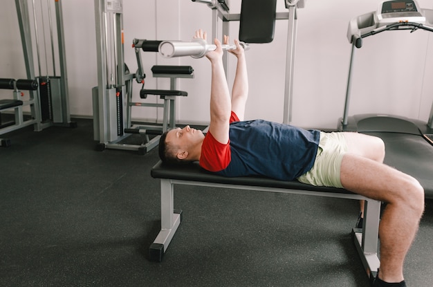 Een man tilt een halter op in de sportschool terwijl hij op een bank ligt. gezonde levensstijl