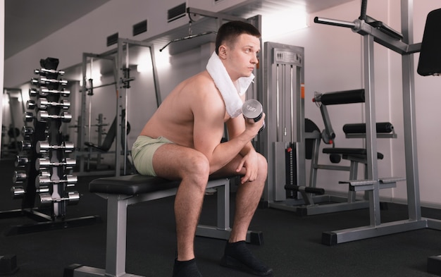 Een man tilt halters op in de fitnessruimte. Een man sport in een sportcentrum. Een persoon geeft om zijn gezondheid. blote romp