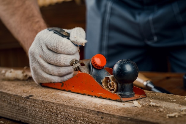 Een man timmerman die zich bezighoudt met houtbewerkingsvliegtuigen het oppervlak van een houten plank in zijn werkplaats met een handvliegtuig Concept van reparatie en constructie