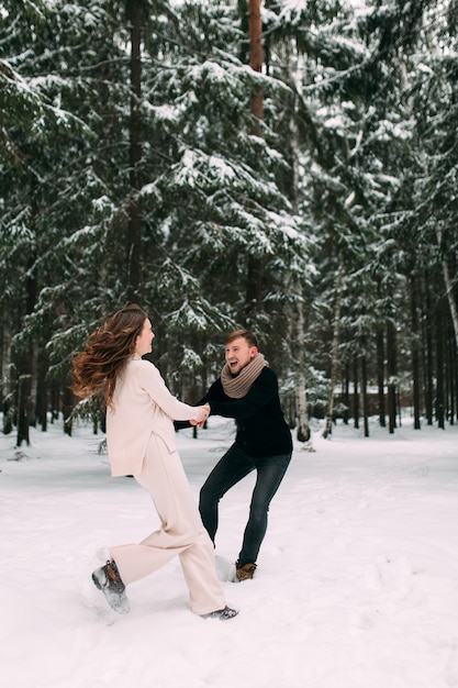 Een man trekt een vrouw achter zich aan in een besneeuwd bos en lacht