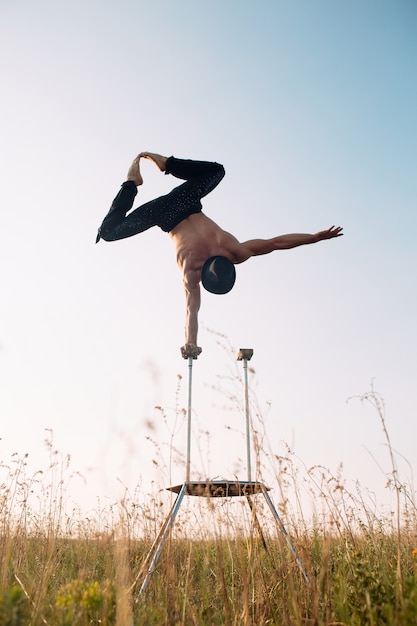 Foto een man van atletische bouw verricht complexe gymnastiekoefeningen in een veld bij zonsondergang