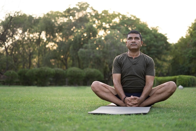 Een man van middelbare leeftijd die yoga doet in een met bomen bedekt park op de internationale yoga dag