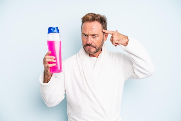 Een man van middelbare leeftijd die zich verward en verbaasd voelt en laat zien dat je gek bent. shampoo fles