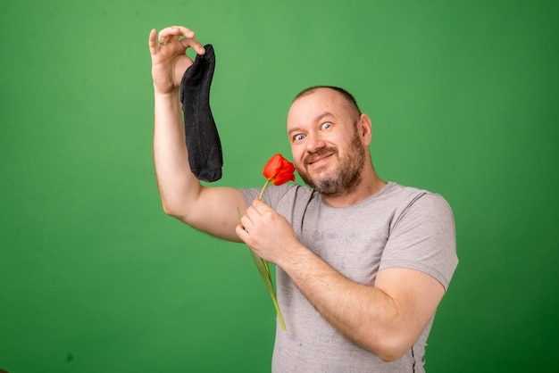 Een man van middelbare leeftijd met een vieze stinkende sok en een verse bloem op een groene achtergrond. Wasserij, hygiëne, stinkende voeten concept.