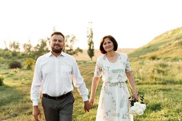 Een man van middelbare leeftijd omhelst een vrouw van Europees voorkomen die bloemen van haar man in haar handen houdt. portret van een verliefd stel bij zonsondergang