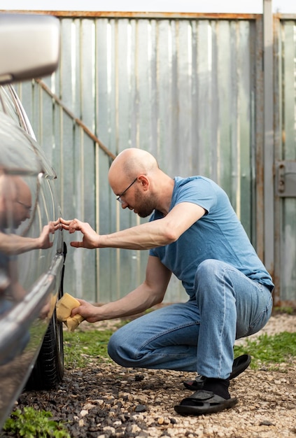 Een man wast een auto door hem af te vegen met een speciale spons op een zonnige dag in zijn achtertuin