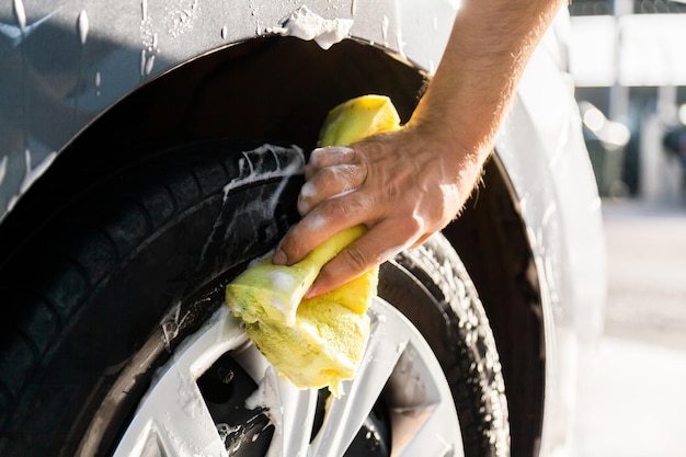 Een man wast zijn auto met schuim bij een close-up van de zelfbedieningsautowasserette met wielen en banden