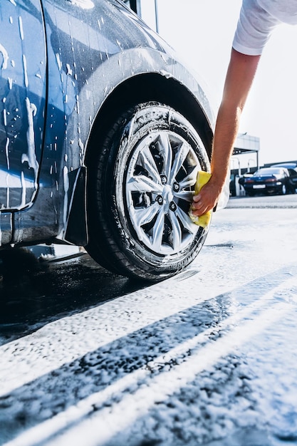 Een man wast zijn auto met schuim bij een close-up van de zelfbedieningsautowasserette met wielen en banden
