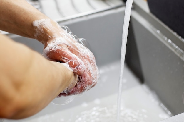 Een man wast zijn handen met zeep onder de kraan onder stromend water close-up