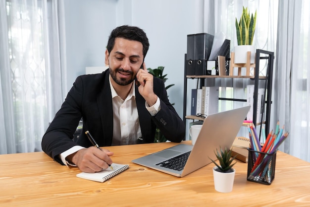 Een man zit aan een bureau en praat aan de telefoon.