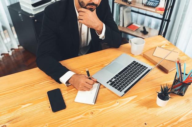 Een man zit aan een bureau met een laptop en een kopje koffie op tafel.