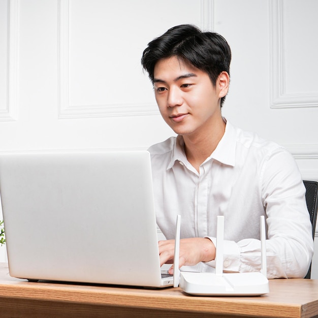 Een man zit aan een bureau met een laptop en een wifi-router.