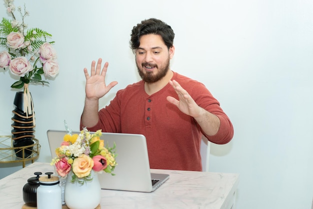 Een man zit aan een tafel met een laptop en een bos bloemen erop.