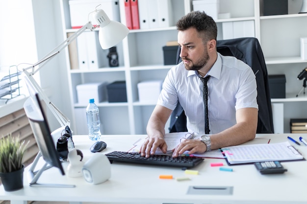 Een man zit aan een tafel op kantoor, werkt met documenten en een computer.