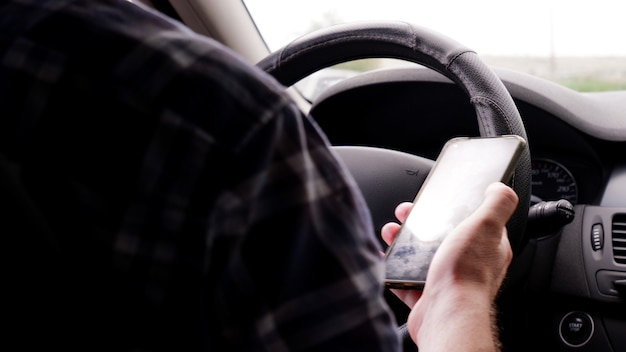 Een man zit in een auto met een mobiele telefoon in zijn hand en schrijft sms'jes tijdens het rijden