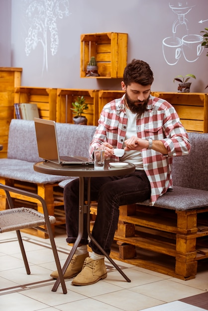 Een man zit in een café en werkt op een laptop.