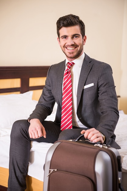 Een man zit in een hotel met een koffer en glimlacht