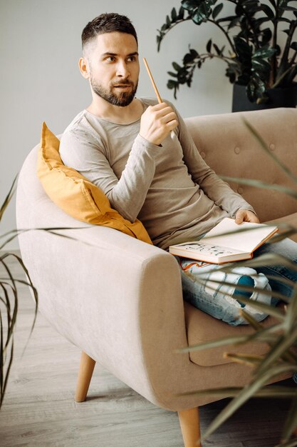 Een man zit op de bank en houdt een schetsboek in zijn handen Een jonge kunstenaar-leraar bespreekt de werkprocessen in de studio Artist's workshop leerproces levensstijl
