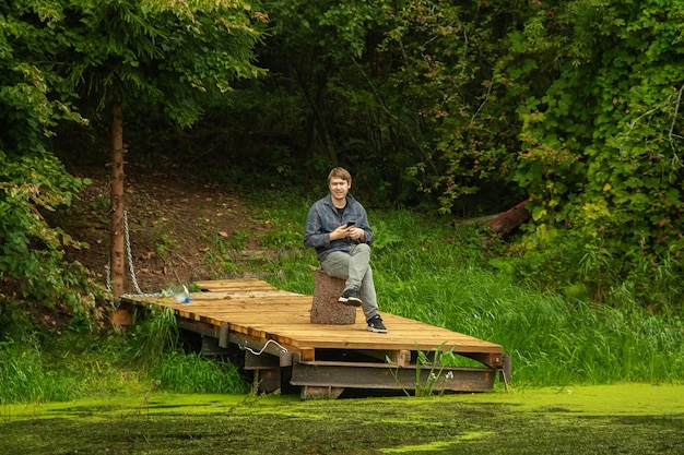 Een man zit op een houten aanlegsteiger op een bosmeer.