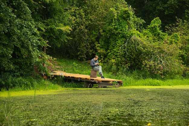 Een man zit op een houten aanlegsteiger op een bosmeer.