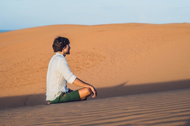 Een man zit op het zand in de woestijn