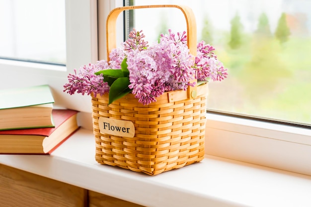 Een mand voor bloemen met een paars boeket seringen staat op de vensterbank en twee boeken. het concept van een goede vakantie op het platteland.