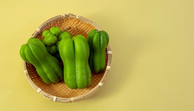 Een mandje groene paprika's zit op een gele achtergrond.